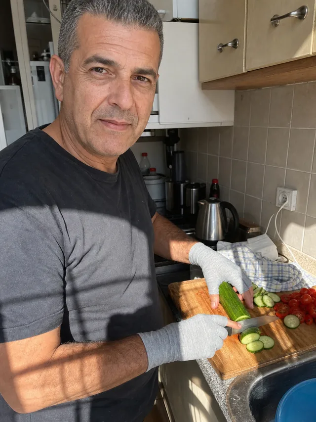 יד לובשת כפפת קומפרסיה אפורה חותכת ירקות במטבח